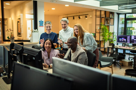 Diverse coworkers celebrating success at computers in modern office
