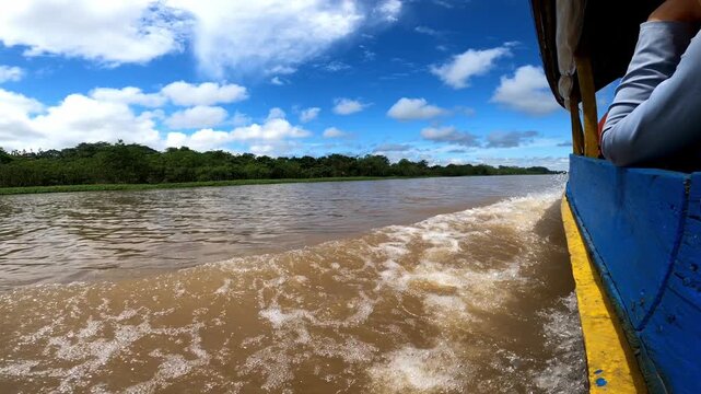 Boat wake splashing on muddy Amazon river water near tropical jungle