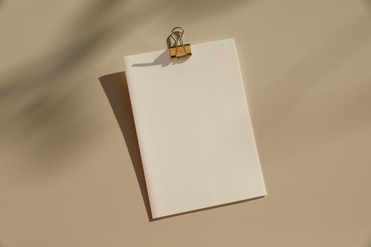 Blank White Notebook Mockup, Gold Metal Binder Clip. Beige Table Background in Natural Sunlight, Long Shadows. Minimal Summer Stationery Template. Branding, Presentation, Office and Creative Design