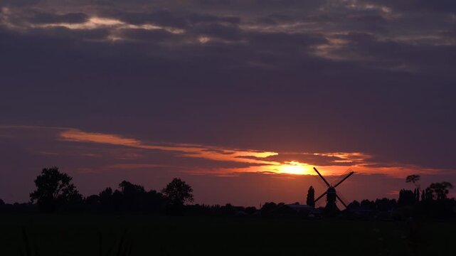 Traditional Dutch Windmill Silhouette Against a Dramatic Summer Sunset in the Netherlands Countryside, Golden Sky over Rural Landscape.