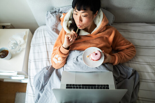 Person relaxing in bed with laptop and cupcake at home