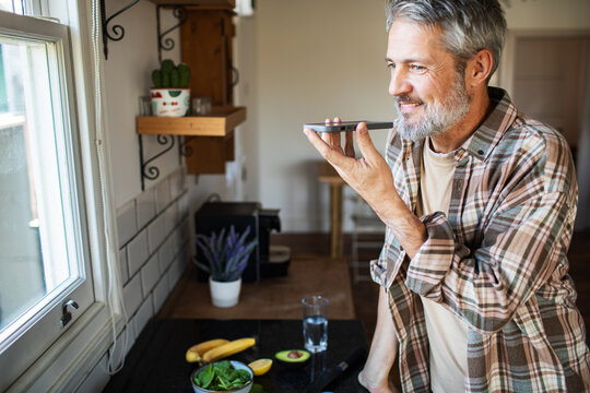 Middle-aged man using voice assistant in home kitchen