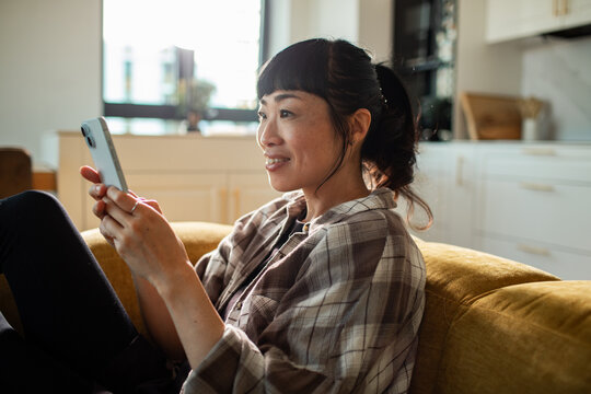 Smiling woman relaxing on sofa using smartphone at home