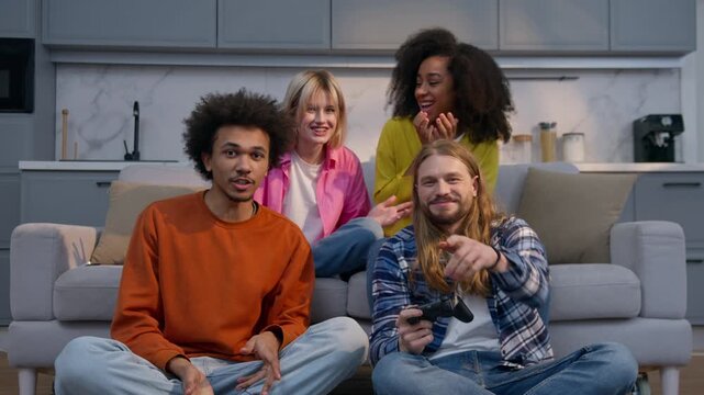 Laughing four diversity multiethnic friends Caucasian women African men playing console video game on couch at home emotional rejoicing competition fun guys girls enjoying victory teamwork joy indoors