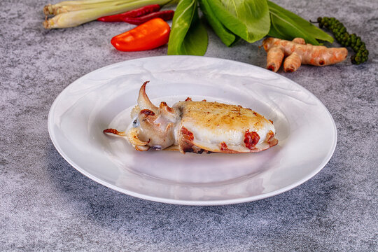 Grilled cuttlefish on white plate with fresh herbs and spices