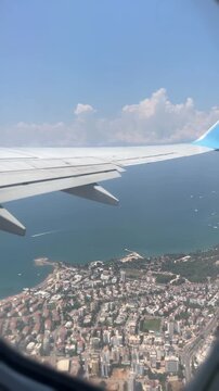 Airplane wing view over the city and sea, with clouds and a blue sky. Travel and aviation concept for business and tourism use.