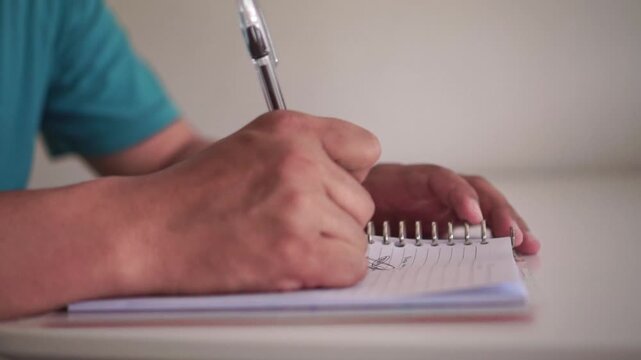Hands scribbling and crossing out words in notebook due to writing mistake. Stress and frustration concept, close-up shot of paper and pen at desk.