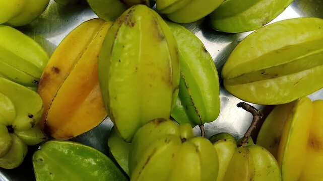 A close up top-down view of a pile of fresh yellow and green star fruits on a metal surface