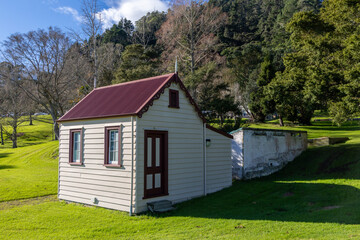 Obraz premium A charming, rustic cottage with a red corrugated iron roof sits on a lush green lawn in a Te Aroha Domain, setting in Te Aroha, New Zealand.