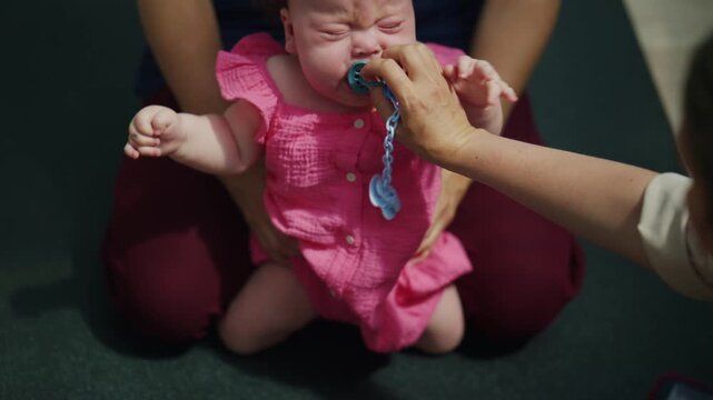 Emotional moment of a baby crying during a supervised developmental exercise session, while a caregiver provides support and comfort during mobility training
