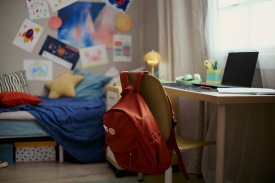 Wide shot of child bedroom showing backpack hanging on chair beside laptop desk, suggesting home study routine and school readiness. Ideal for education, back to school, parenting campaigns