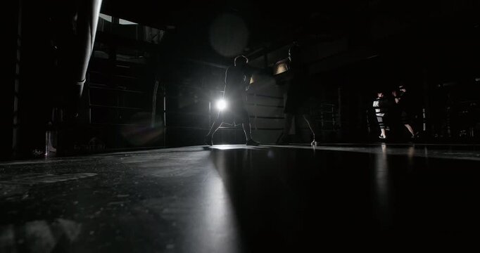 Wide cinematic shot of a boxer training with a coach in a dark boxing gym. Intense coaching session focused on boxing technique, footwork, speed, endurance and fight preparation under dramatic