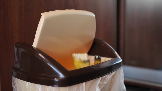 A banana peel slowly falls into a kitchen trash bin.