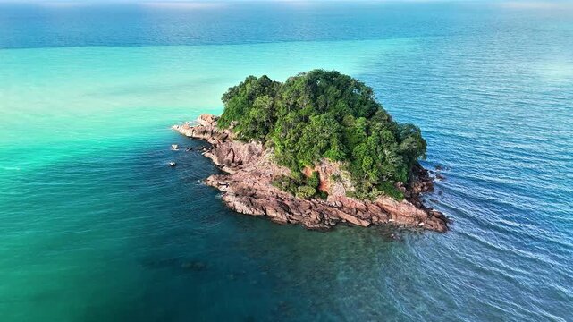 Aerial drone view of a small tropical island surrounded by turquoise ocean beside a hidden beach with granite shoreline under clear blue sky paradise