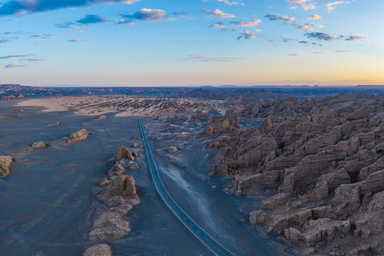 Aerial view of an empty winding asphalt road through yardang landforms at sunset, Dahaidao, Xinjiang, China