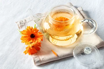 Calendula tea. Vibrant orange marigold flowers infusing in a clear glass teapot © laplateresca