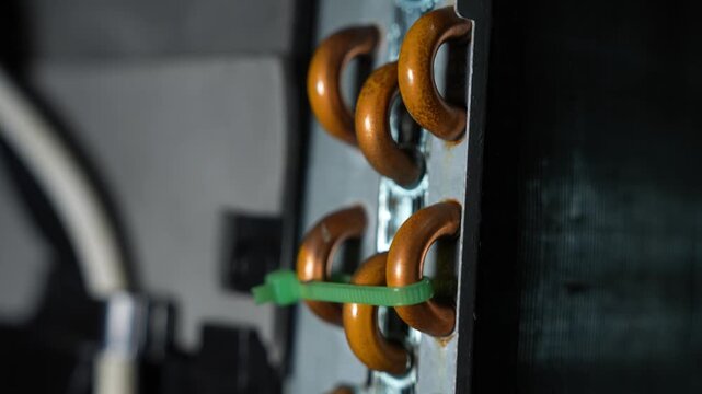 Close-up of copper pipe loops on industrial equipment, secured with a green cable tie. Dark background and shallow focus create a technical, repair and maintenance feel