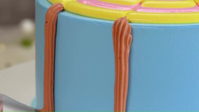 Piping brown frosting stripes down the side of a blue cake close-up