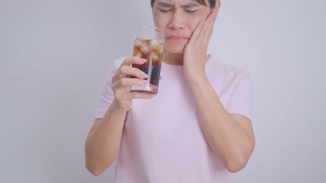 Woman drinking carbonated ice water and feeling sensitive teeth to cold pain, hand holding glass of cold sparkling water. dental health problem from soda acidity, toothache and oral care concept