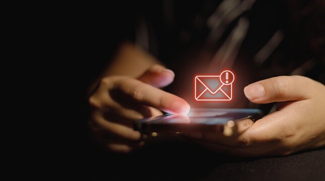 Person checking digital email notification on a smartphone screen in a dark environment with glowing red alert icon