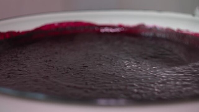 Chef Stirring Dark Purple Berry Puree in a Large Round Metal Mixing Bowl