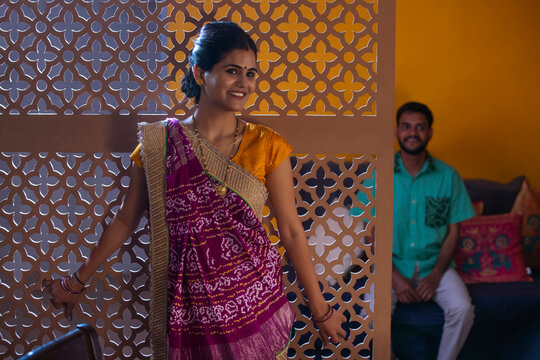 Portrait of smiling Gujrati woman standing and her husband sitting behind
