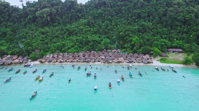 Aerial view of traditional stilt village on a tropical island with turquoise water and numerous boats.