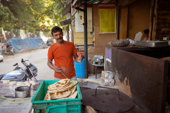 Cook of a local roadside restaurant or a dhaba, making bread or a roti,in a clay wood fired oven or a  tandoor  