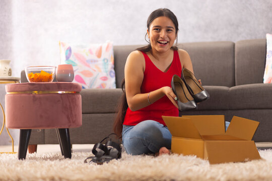 Happy teenage girl unpacking shoes from cardboard box after online shopping