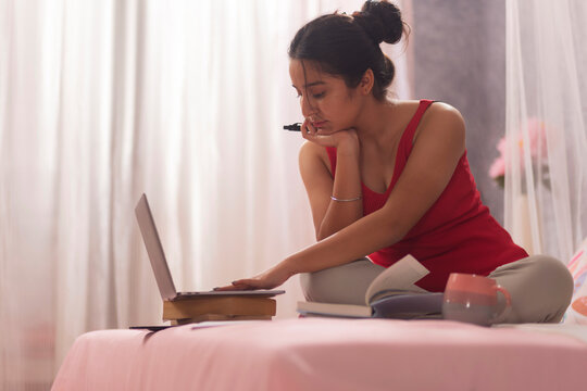 Portrait of teenage girl studying with laptop in bedroom