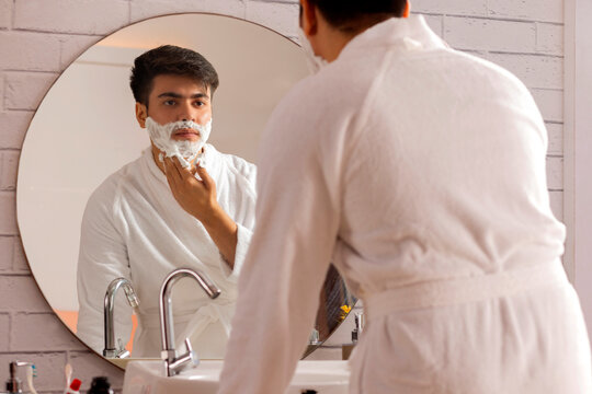 Young man applying shaving cream to his face in a bathroom at home