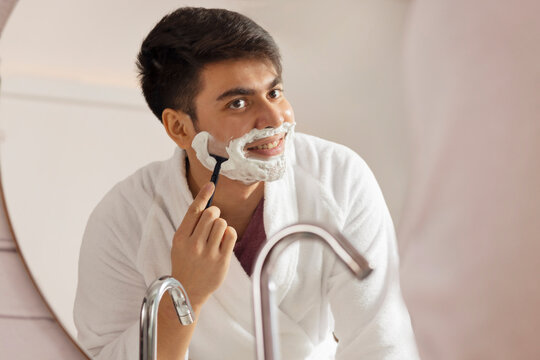 Young man shaving in front of bathroom mirror