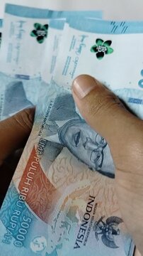 A close-up of a person counting Indonesian 50,000 rupiah banknotes by hand, representing personal finance, cash transactions, savings, budgeting, banking, business payments, and the Indonesian economy
