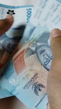 A close-up of a person counting Indonesian 50,000 rupiah banknotes by hand, representing personal finance, cash transactions, savings, budgeting, banking, business payments, and the Indonesian economy