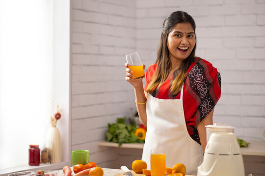 Side view of a cheerful woman drinking orange juice in kitchen