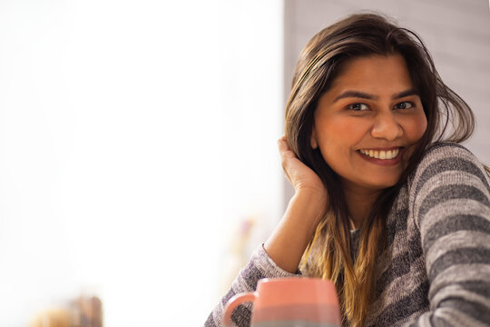 Close-up portrait of smiling woman drinking coffee at home