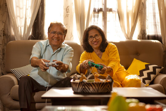 Mature couple playing video game sitting together on sofa in living room