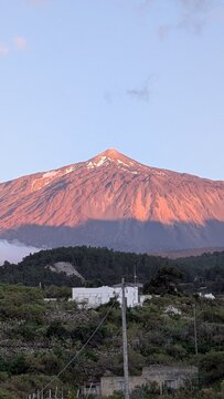 Scenic view of Mount Teide volcano peak in Tenerife during golden hour, majestic mountain landscape with green hills under a bright blue sky with soft white clouds, beautiful nature travel background