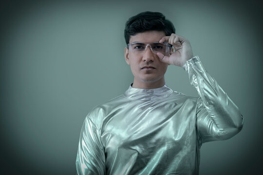 A man wearing silver,futuristic clothes holding glasses and looking at camera,future technology concept