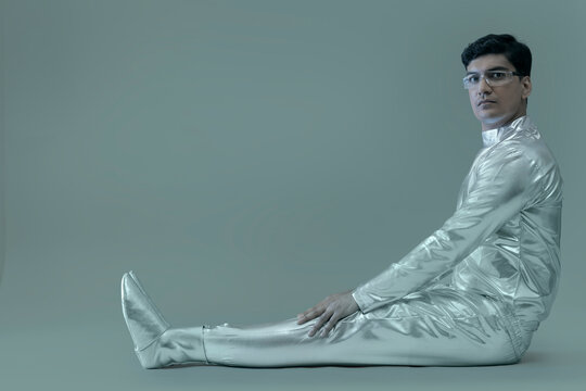 side view of a man wearing silver dress sitting on a grey backdrop,future technology concept. 