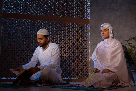 Muslim man reading Koran and woman praying with holding a prayer beads
