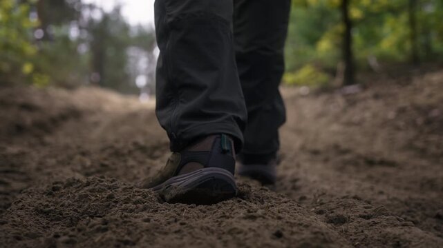 Slow motion low angle gimbal follow shot of man hiking uphill on deep sandy forest trail. Cinematic tracking footage capturing trekking, endurance, outdoor adventure and nature exploration