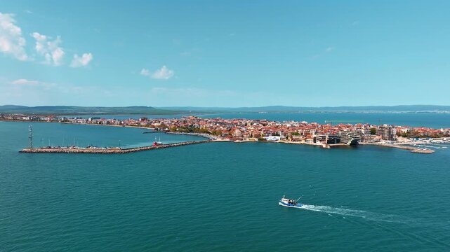 Small fishing boat cruising deep blue water near Pomorie peninsula coast harbor pier summer sunny landscape aerial drone view Bulgaria Black sea travel background.