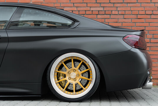 Rear side view of tuned BMW 4 Series F32 coupe with custom golden SSR Professor MS3 forged alloy wheel rim, luxury matte black stance automobile parked near brick wall, automotive tuning industry. 