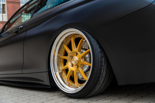 Rear side view of tuned BMW 4 Series F32 coupe with custom golden SSR Professor MS3 forged alloy wheel rim, luxury matte black stance automobile parked near brick wall, automotive tuning industry. 