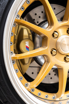 Macro close up of a luxury custom gold alloy wheel rim and tire with a BMW M brake caliper, drilled brake disc rotor. Macro close up of a custom gold SSR alloy wheel rim center cap with bolts. 