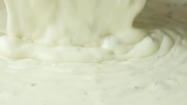 Creamy tartar sauce pouring into a bowl close up