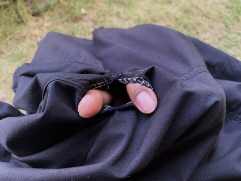 Two fingers sticking out through a torn hole on black pants seam. frayed threads.