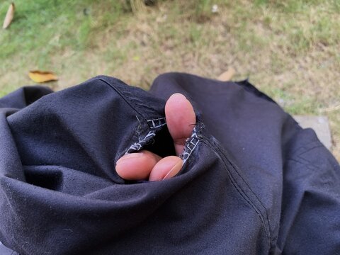 Three fingers sticking out through a torn hole on black pants seam. damaged clothing material.