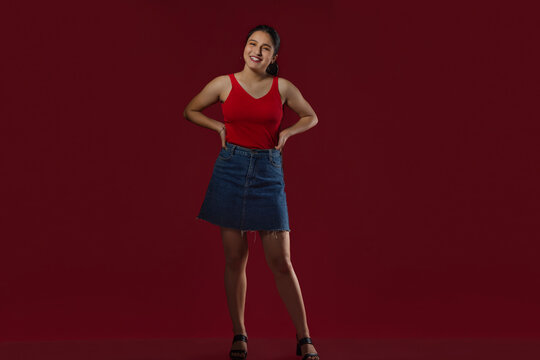 Teenage girl standing with hands on waist against maroon background